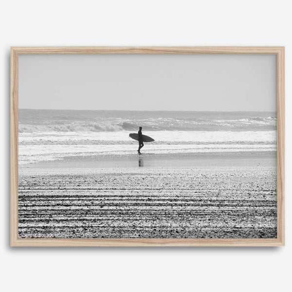 Black and white surfer photography showing a lone surfer on the beach, with waves in the background, capturing minimalist coastal beauty.