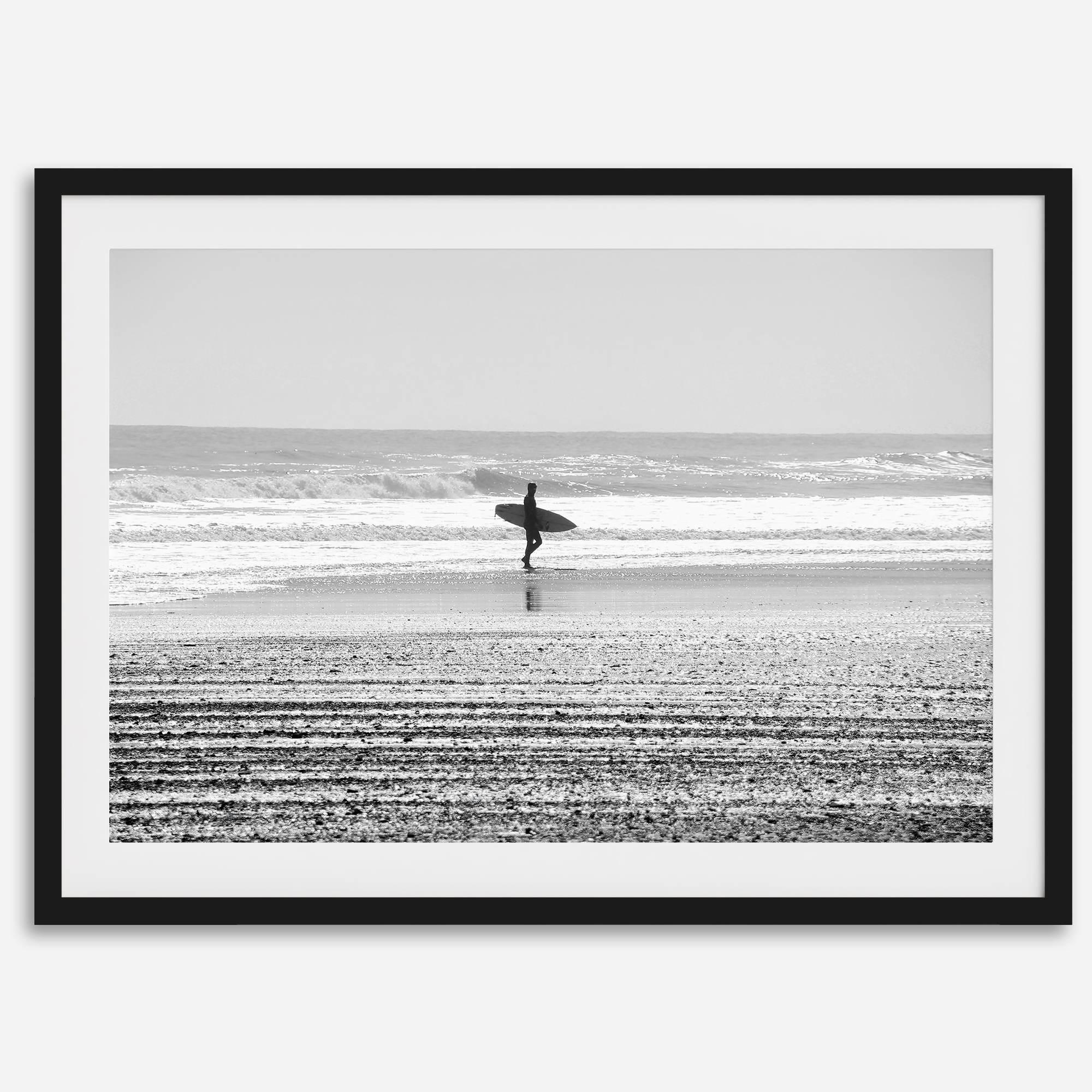 Black and white surfer photography showing a lone surfer on the beach, with waves in the background, capturing minimalist coastal beauty.
