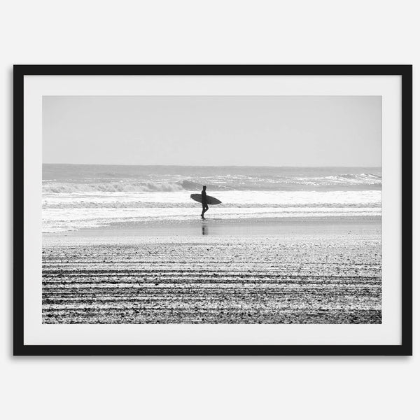 Black and white surfer photography showing a lone surfer on the beach, with waves in the background, capturing minimalist coastal beauty.