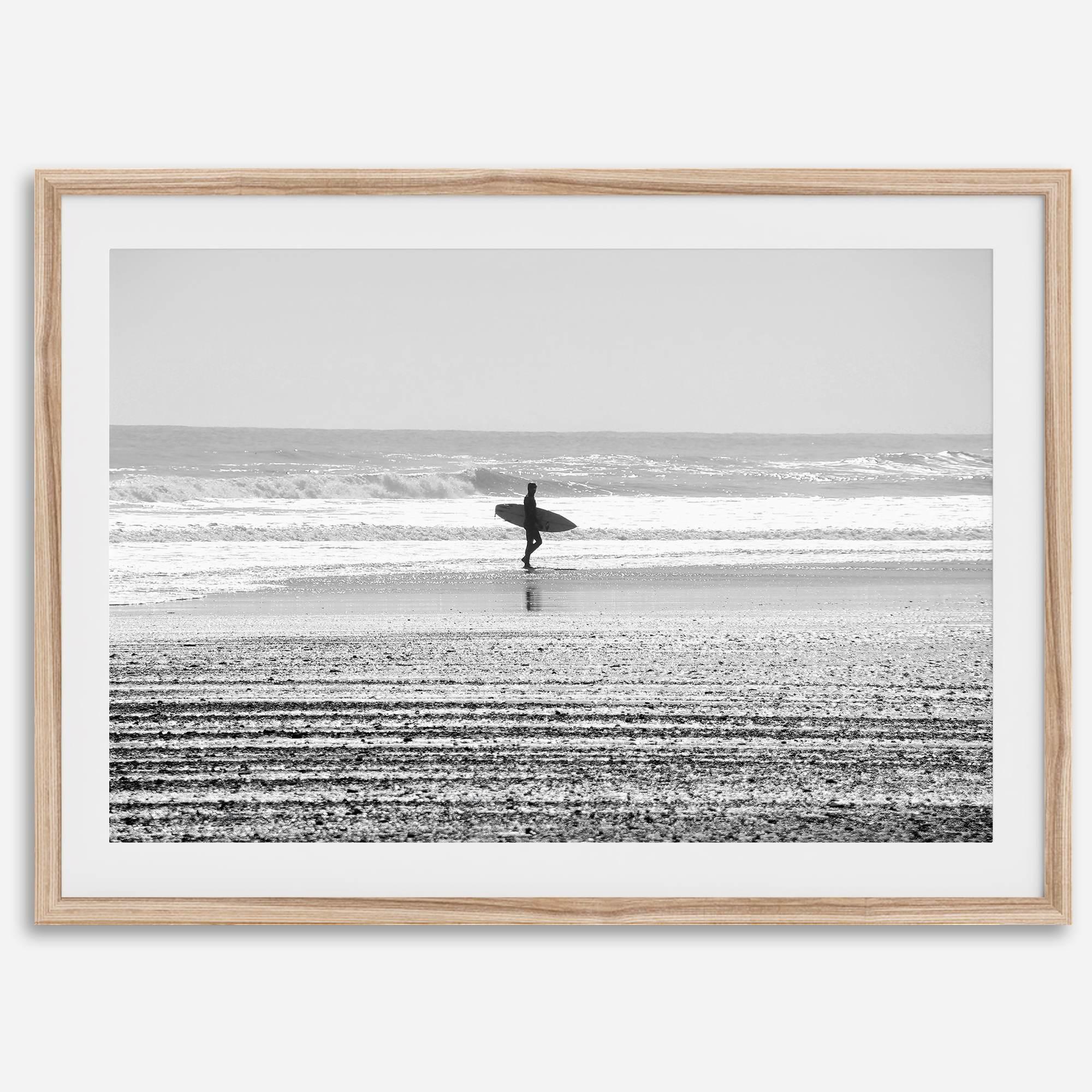Black and white surfer photography showing a lone surfer on the beach, with waves in the background, capturing minimalist coastal beauty.