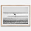 Black and white surfer photography showing a lone surfer on the beach, with waves in the background, capturing minimalist coastal beauty.