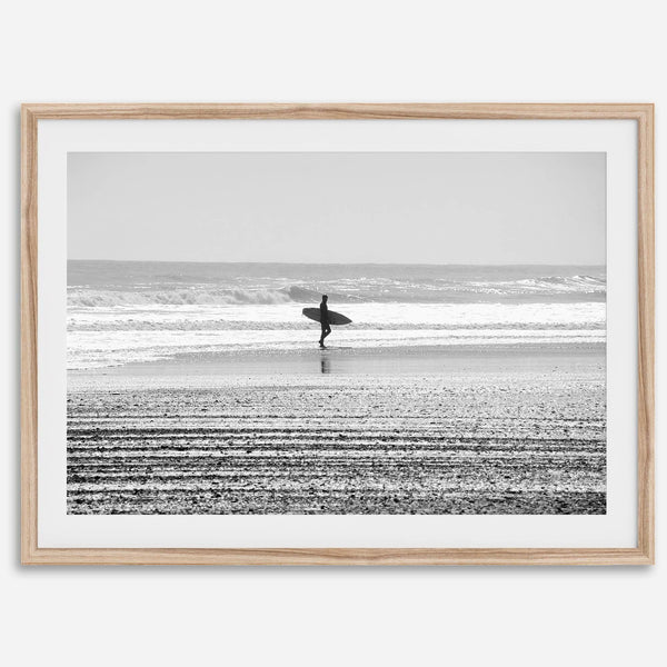Black and white surfer photography showing a lone surfer on the beach, with waves in the background, capturing minimalist coastal beauty.