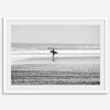Black and white surfer photography showing a lone surfer on the beach, with waves in the background, capturing minimalist coastal beauty.