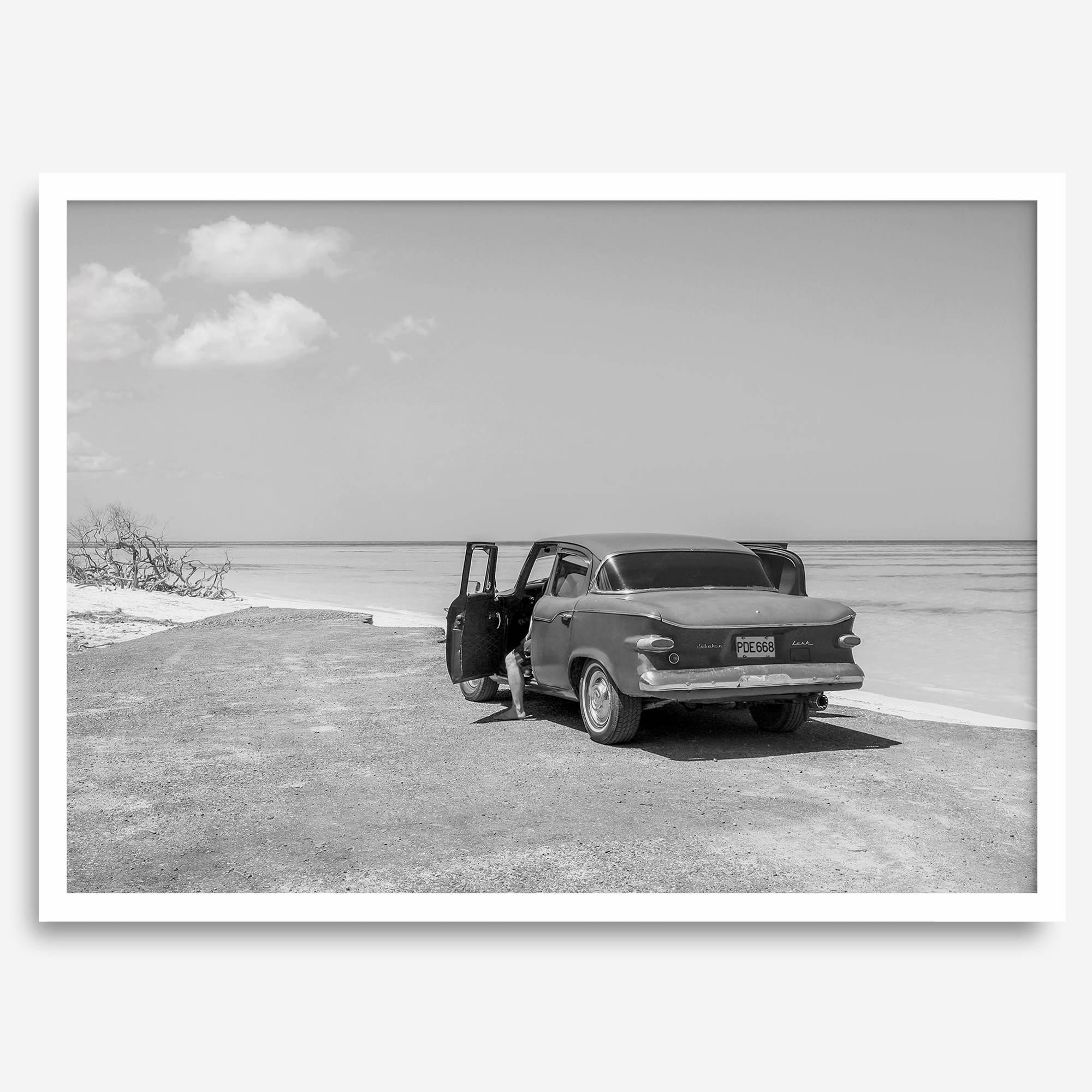 Black and white vintage beach print featuring a classic car parked at the edge of the ocean, capturing a retro coastal scene with timeless charm.