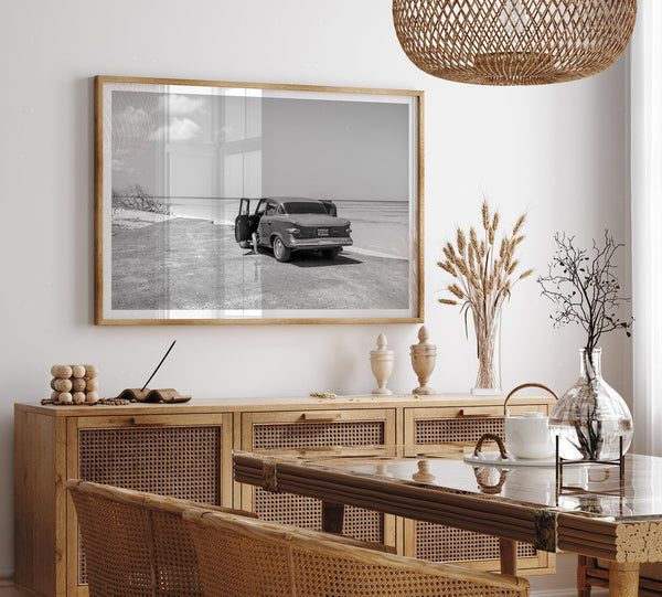 Black and white vintage beach print featuring a classic car parked at the edge of the ocean, capturing a retro coastal scene with timeless charm.