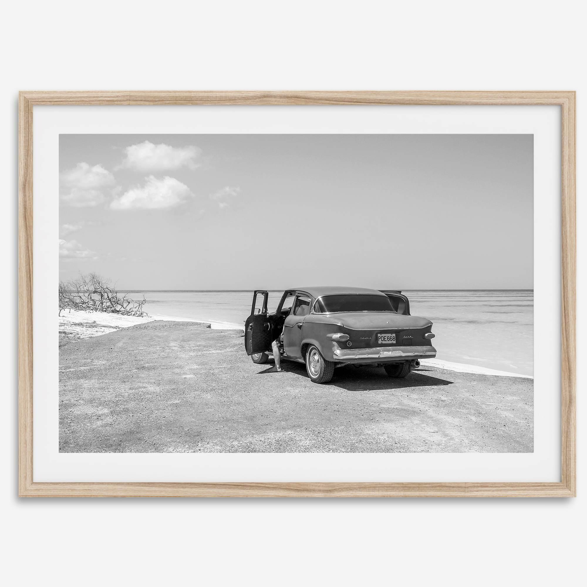 Black and white vintage beach print featuring a classic car parked at the edge of the ocean, capturing a retro coastal scene with timeless charm.