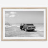 Black and white vintage beach print featuring a classic car parked at the edge of the ocean, capturing a retro coastal scene with timeless charm.