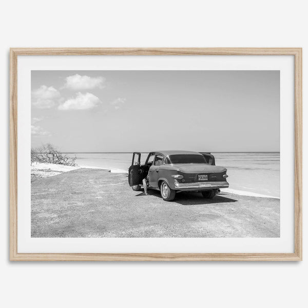 Black and white vintage beach print featuring a classic car parked at the edge of the ocean, capturing a retro coastal scene with timeless charm.