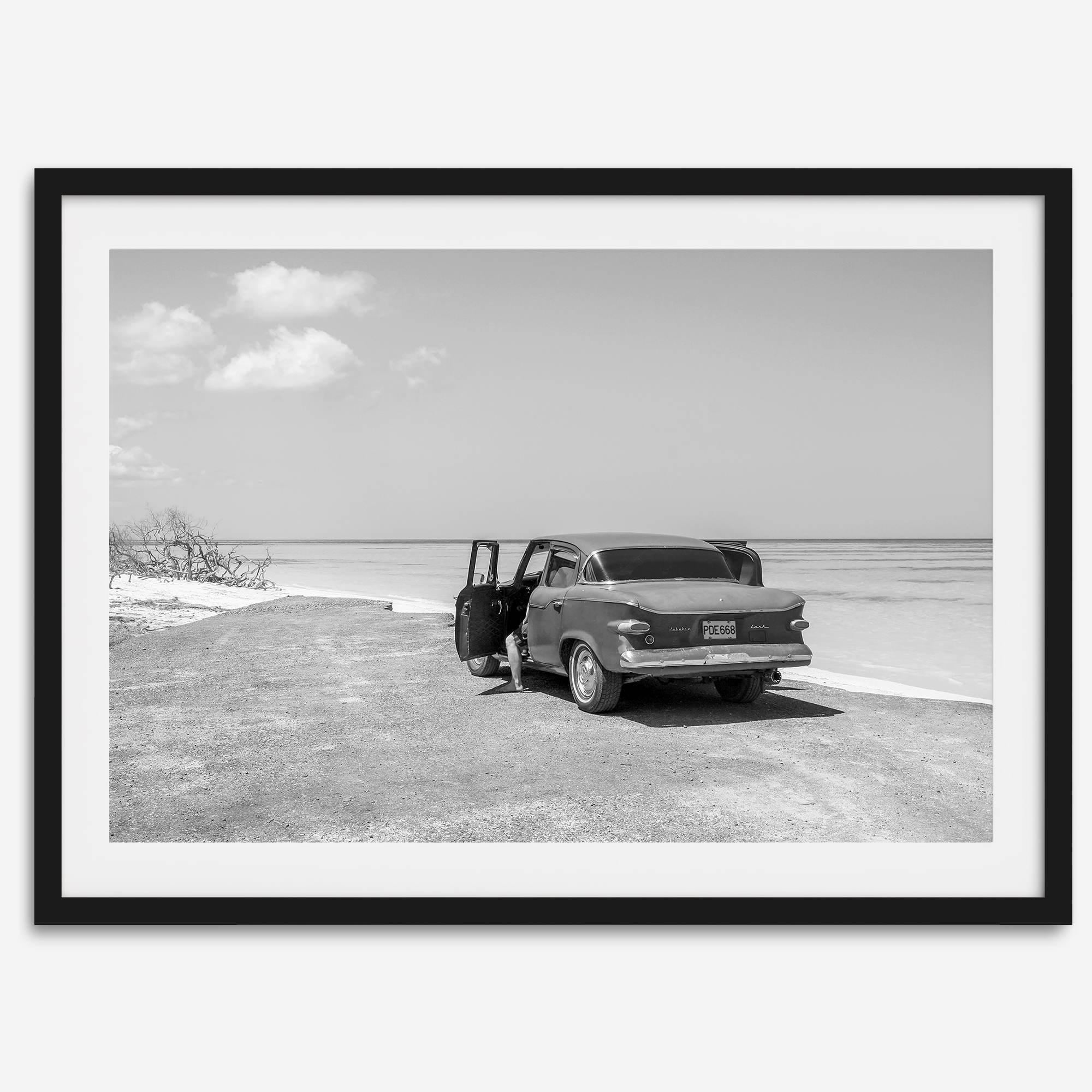 Black and white vintage beach print featuring a classic car parked at the edge of the ocean, capturing a retro coastal scene with timeless charm.