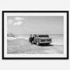 Black and white vintage beach print featuring a classic car parked at the edge of the ocean, capturing a retro coastal scene with timeless charm.