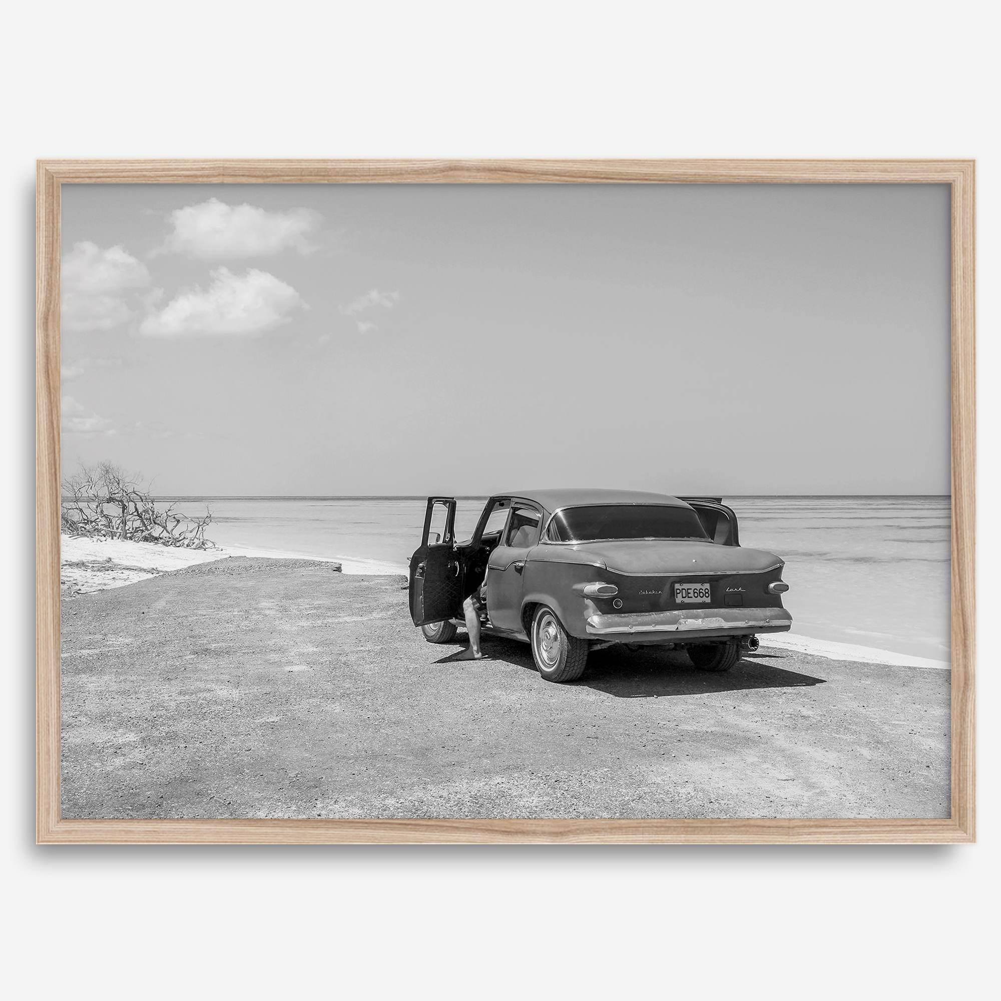 Black and white vintage beach print featuring a classic car parked at the edge of the ocean, capturing a retro coastal scene with timeless charm.