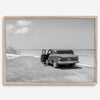 Black and white vintage beach print featuring a classic car parked at the edge of the ocean, capturing a retro coastal scene with timeless charm.