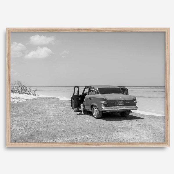 Black and white vintage beach print featuring a classic car parked at the edge of the ocean, capturing a retro coastal scene with timeless charm.