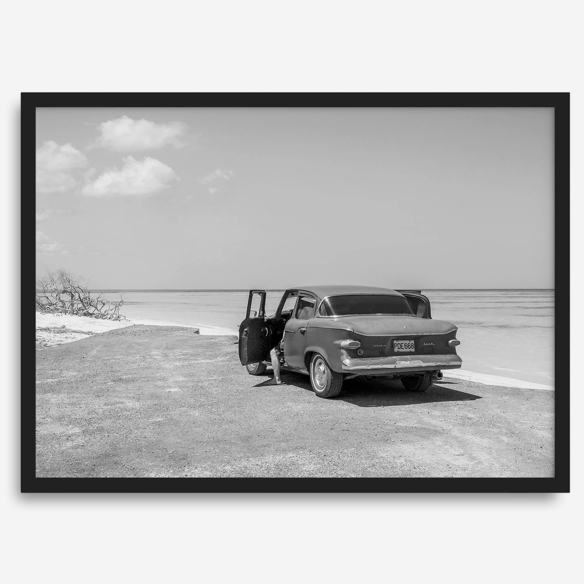 Black and white vintage beach print featuring a classic car parked at the edge of the ocean, capturing a retro coastal scene with timeless charm.