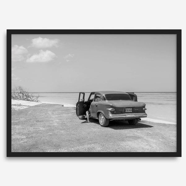 Black and white vintage beach print featuring a classic car parked at the edge of the ocean, capturing a retro coastal scene with timeless charm.
