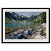 A framed fine art landscape print of a crystal-clear blue lake in Washington State. The tranquil water reveals colorful rocks beneath the surface, with snow-capped mountains towering in the distance.