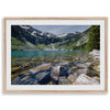 A framed fine art landscape print of a crystal-clear blue lake in Washington State. The tranquil water reveals colorful rocks beneath the surface, with snow-capped mountains towering in the distance.