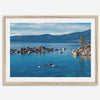 A fine art Lake Tahoe print showcasing a lone stand-up paddle peacefully gliding across the clear water lake near the huge rocks of Sand Harbor Beach with the backdrop of the Sierra Nevada mountains.