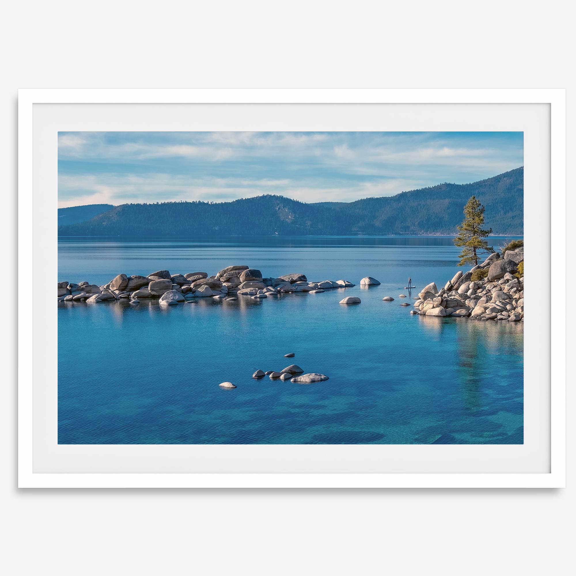 A fine art Lake Tahoe print showcasing a lone stand-up paddle peacefully gliding across the clear water lake near the huge rocks of Sand Harbor Beach with the backdrop of the Sierra Nevada mountains.
