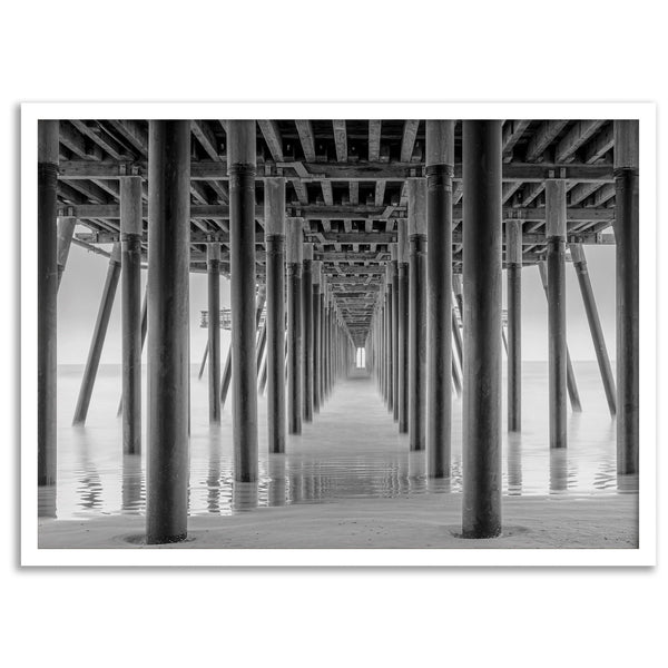 A large fine art abstract black and white beach pier print This stunning beach wall art shows the symmetric structure of the pier with the ocean water gently caressing the pier and beach.