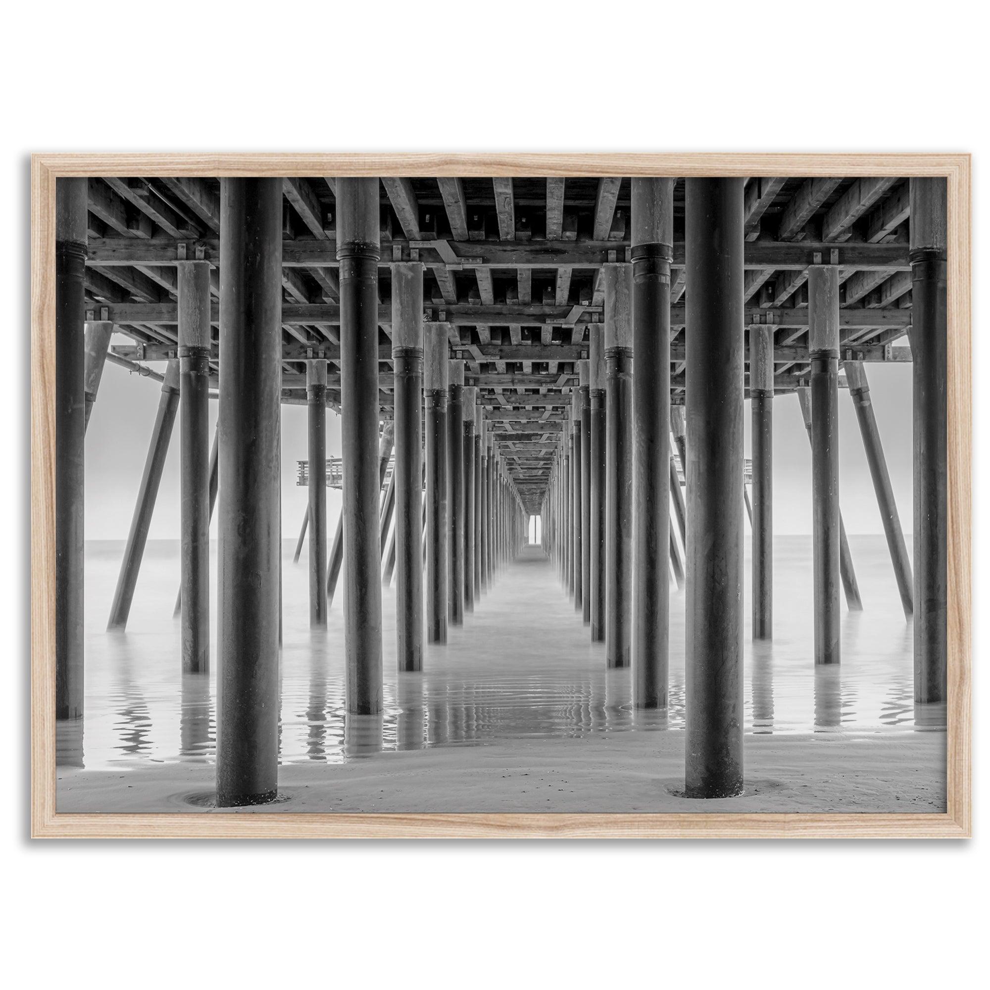 A large fine art abstract black and white beach pier print This stunning beach wall art shows the symmetric structure of the pier with the ocean water gently caressing the pier and beach.