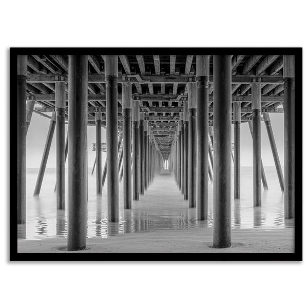 A large fine art abstract black and white beach pier print This stunning beach wall art shows the symmetric structure of the pier with the ocean water gently caressing the pier and beach.