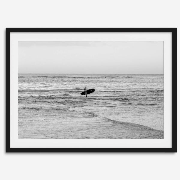 A fine art photography print capturing a female surfer walking back from the ocean at sunset with waves breaking in the foreground, capturing the end of a surf session.