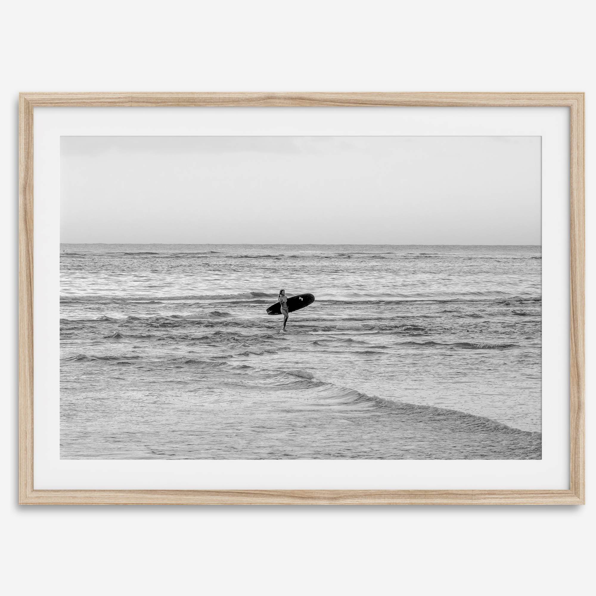 A fine art photography print capturing a female surfer walking back from the ocean at sunset with waves breaking in the foreground, capturing the end of a surf session.