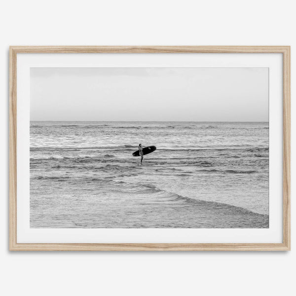 A fine art photography print capturing a female surfer walking back from the ocean at sunset with waves breaking in the foreground, capturing the end of a surf session.