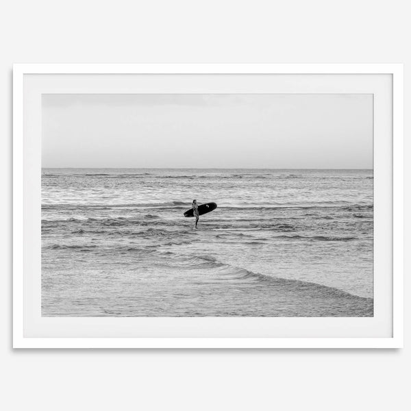 A fine art photography print capturing a female surfer walking back from the ocean at sunset with waves breaking in the foreground, capturing the end of a surf session.