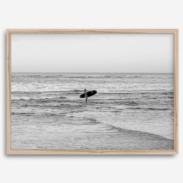 A fine art photography print capturing a female surfer walking back from the ocean at sunset with waves breaking in the foreground, capturing the end of a surf session.