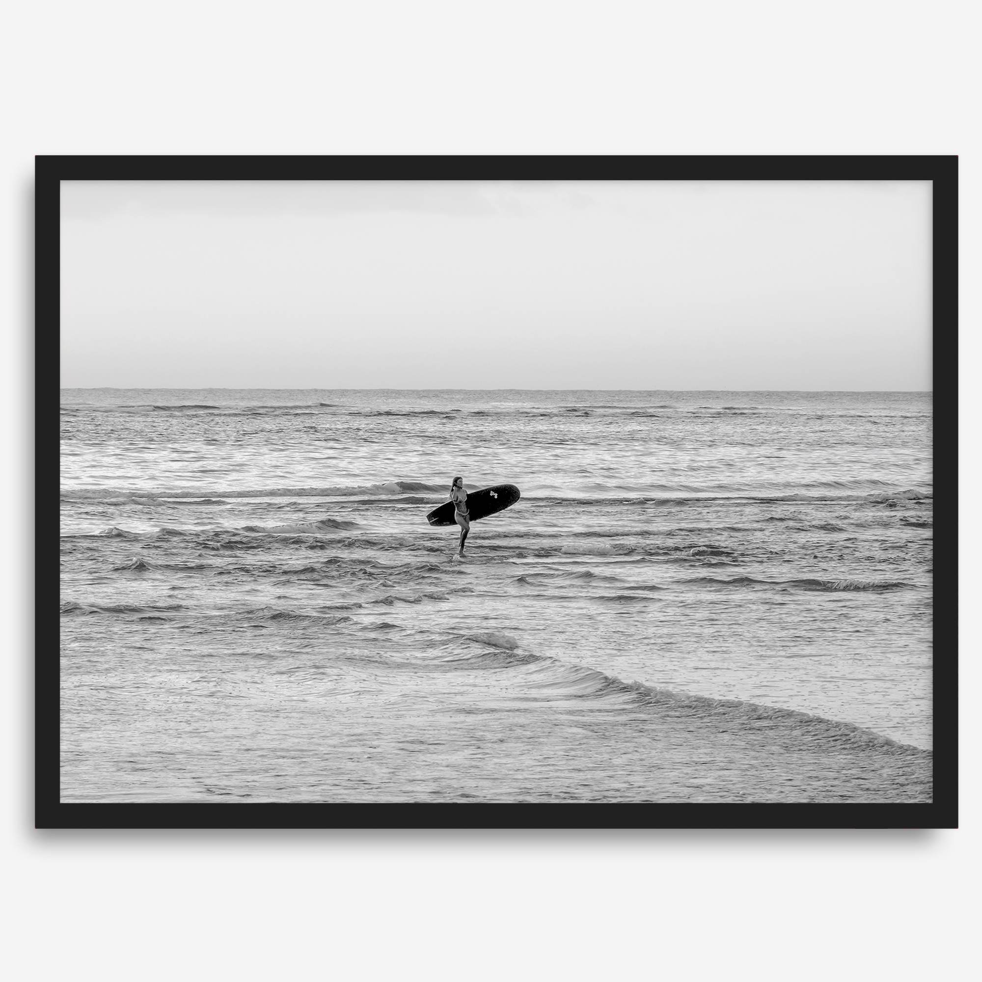 A fine art photography print capturing a female surfer walking back from the ocean at sunset with waves breaking in the foreground, capturing the end of a surf session.