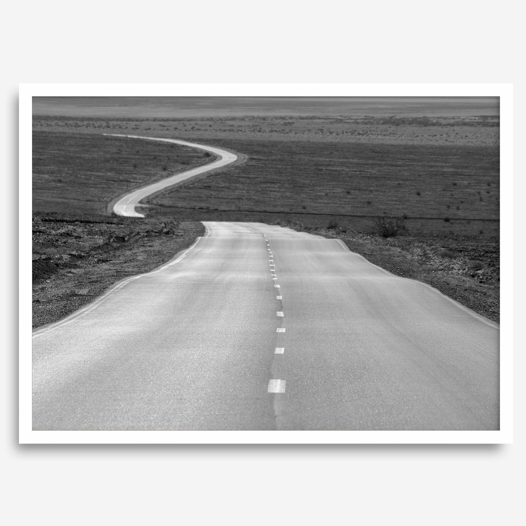 Black and white fine art photo of a winding desert road stretching through a vast minimalist landscape.