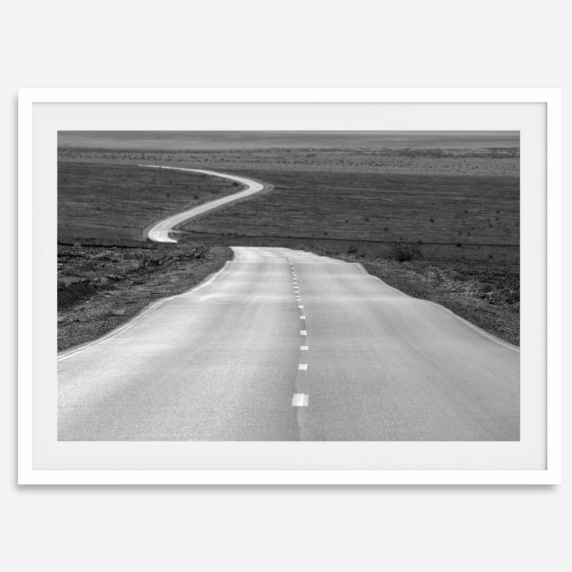 Black and white fine art photo of a winding desert road stretching through a vast minimalist landscape.