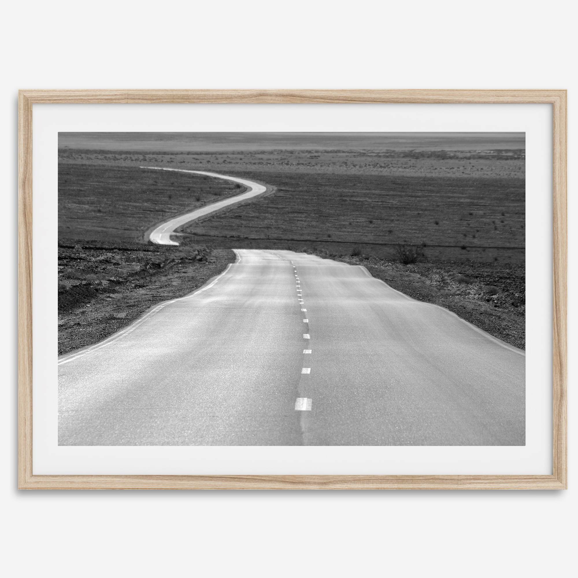 Black and white fine art photo of a winding desert road stretching through a vast minimalist landscape.
