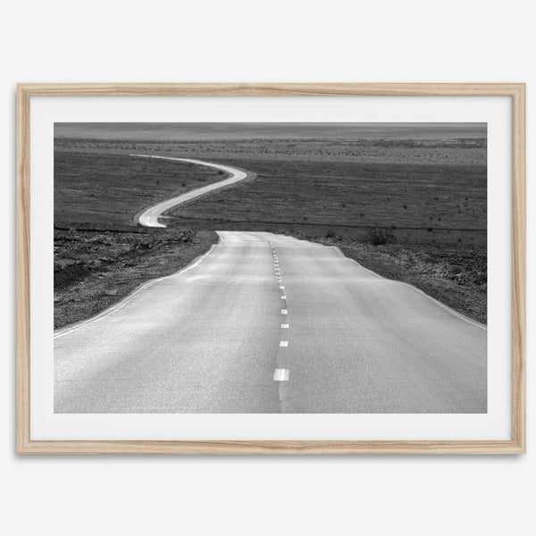Black and white fine art photo of a winding desert road stretching through a vast minimalist landscape.