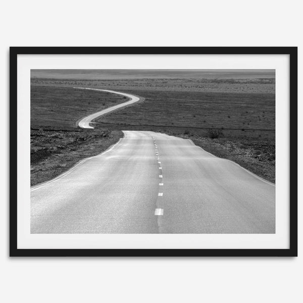 Black and white fine art photo of a winding desert road stretching through a vast minimalist landscape.