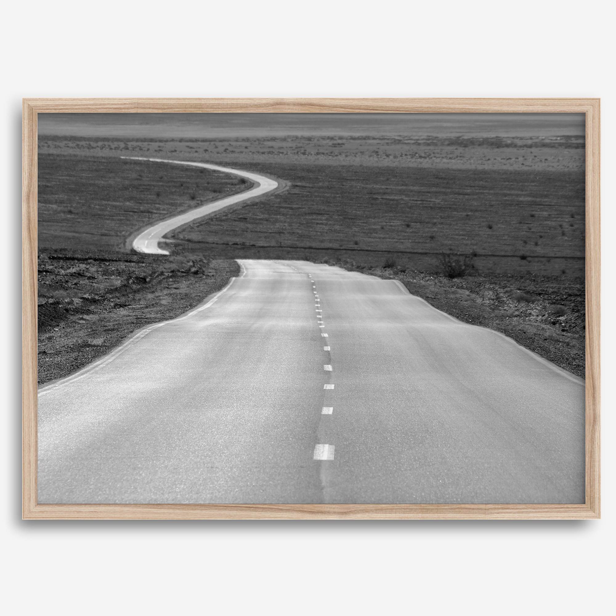 Black and white fine art photo of a winding desert road stretching through a vast minimalist landscape.