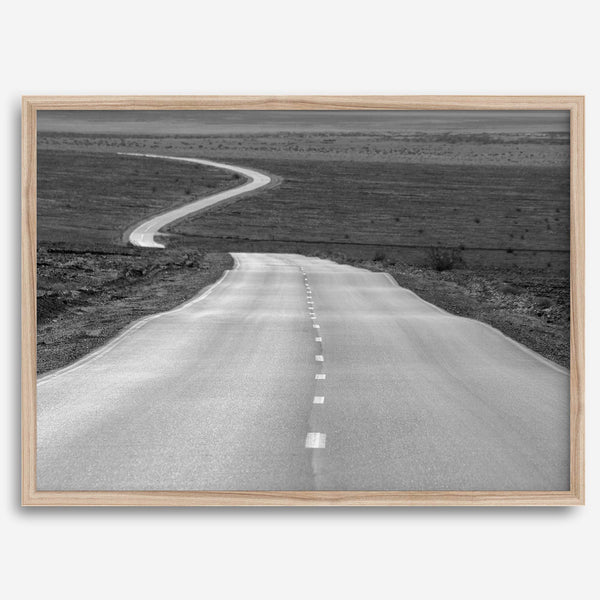 Black and white fine art photo of a winding desert road stretching through a vast minimalist landscape.
