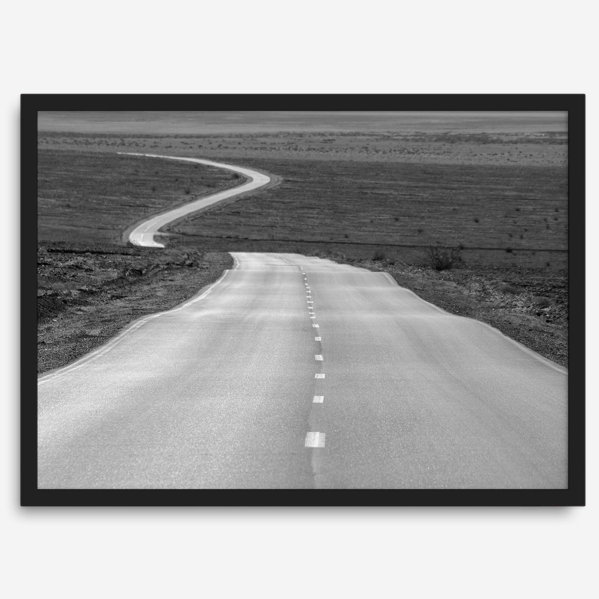 Black and white fine art photo of a winding desert road stretching through a vast minimalist landscape.