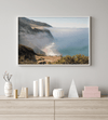 A fine art print of a misty beach in Big Sur, California. Waves crash against the shore as fog drapes over the rugged coastal cliffs, creating a serene, atmospheric scene