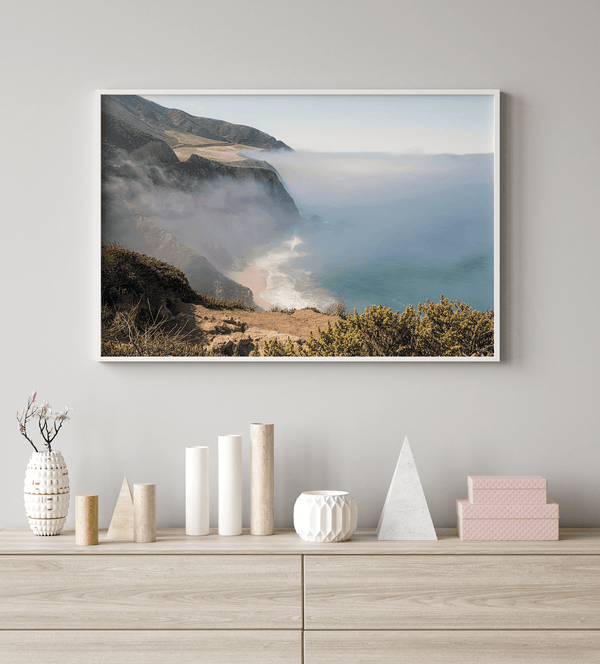 A fine art print of a misty beach in Big Sur, California. Waves crash against the shore as fog drapes over the rugged coastal cliffs, creating a serene, atmospheric scene