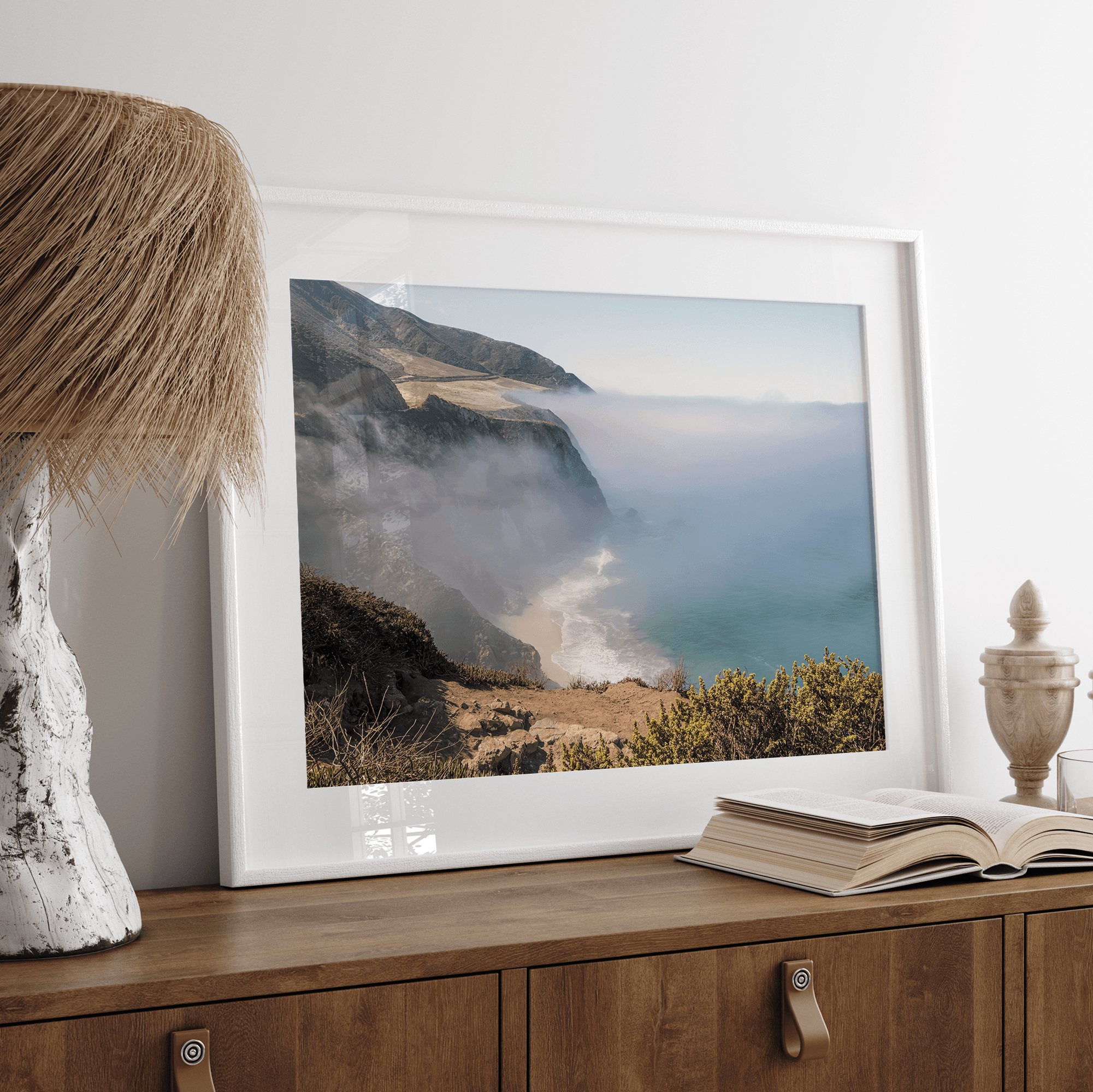 A fine art print of a misty beach in Big Sur, California. Waves crash against the shore as fog drapes over the rugged coastal cliffs, creating a serene, atmospheric scene