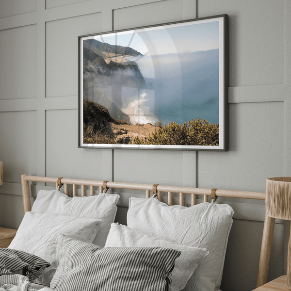 A fine art print of a misty beach in Big Sur, California. Waves crash against the shore as fog drapes over the rugged coastal cliffs, creating a serene, atmospheric scene