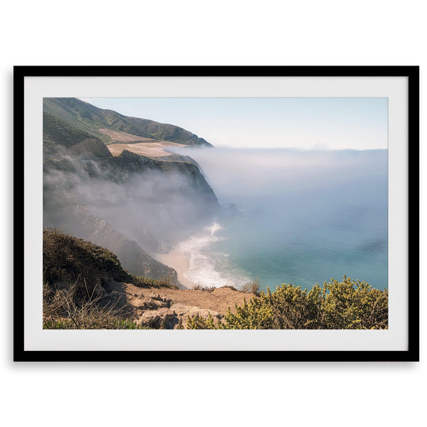 A fine art print of a misty beach in Big Sur, California. Waves crash against the shore as fog drapes over the rugged coastal cliffs, creating a serene, atmospheric scene