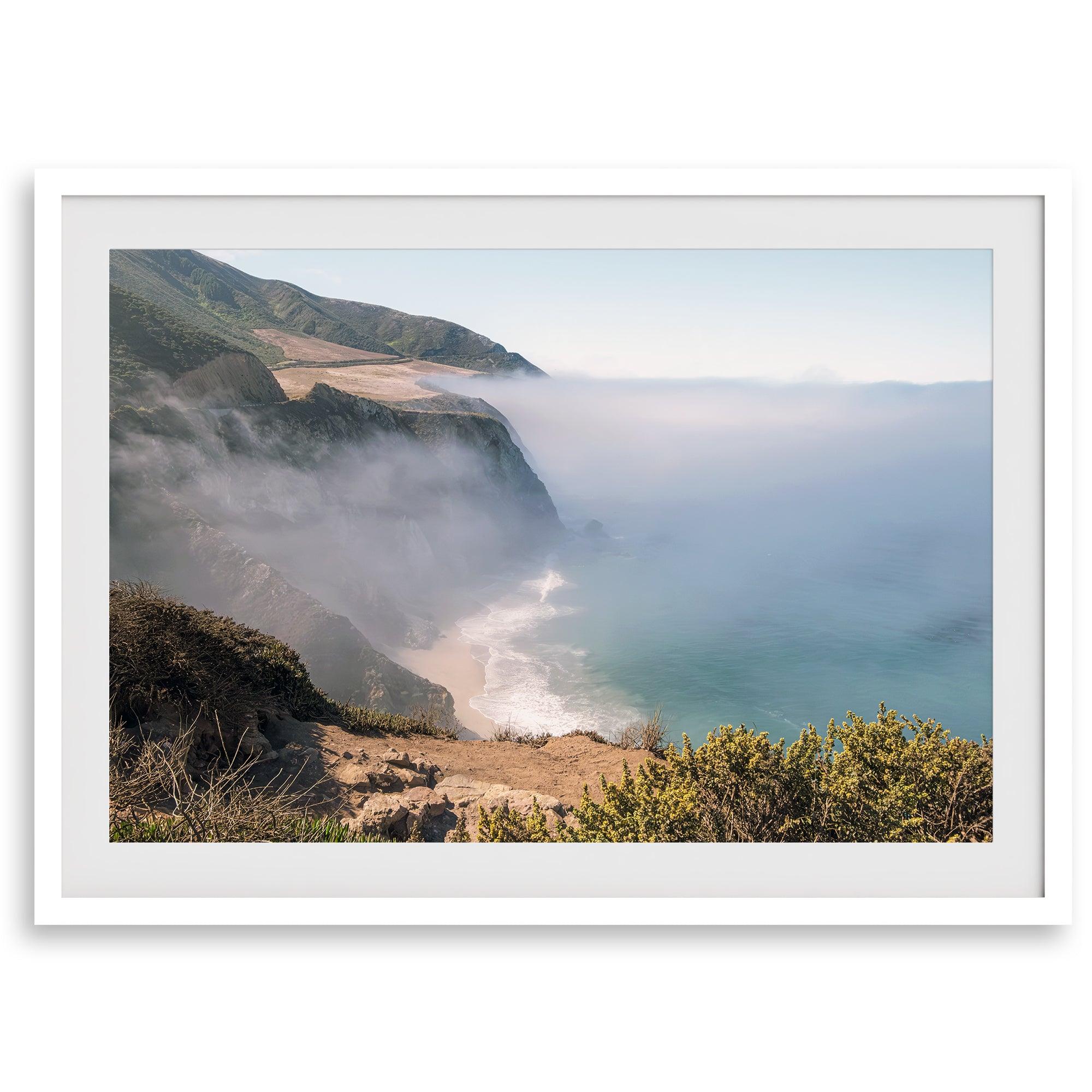 A fine art print of a misty beach in Big Sur, California. Waves crash against the shore as fog drapes over the rugged coastal cliffs, creating a serene, atmospheric scene