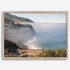 A fine art print of a misty beach in Big Sur, California. Waves crash against the shore as fog drapes over the rugged coastal cliffs, creating a serene, atmospheric scene