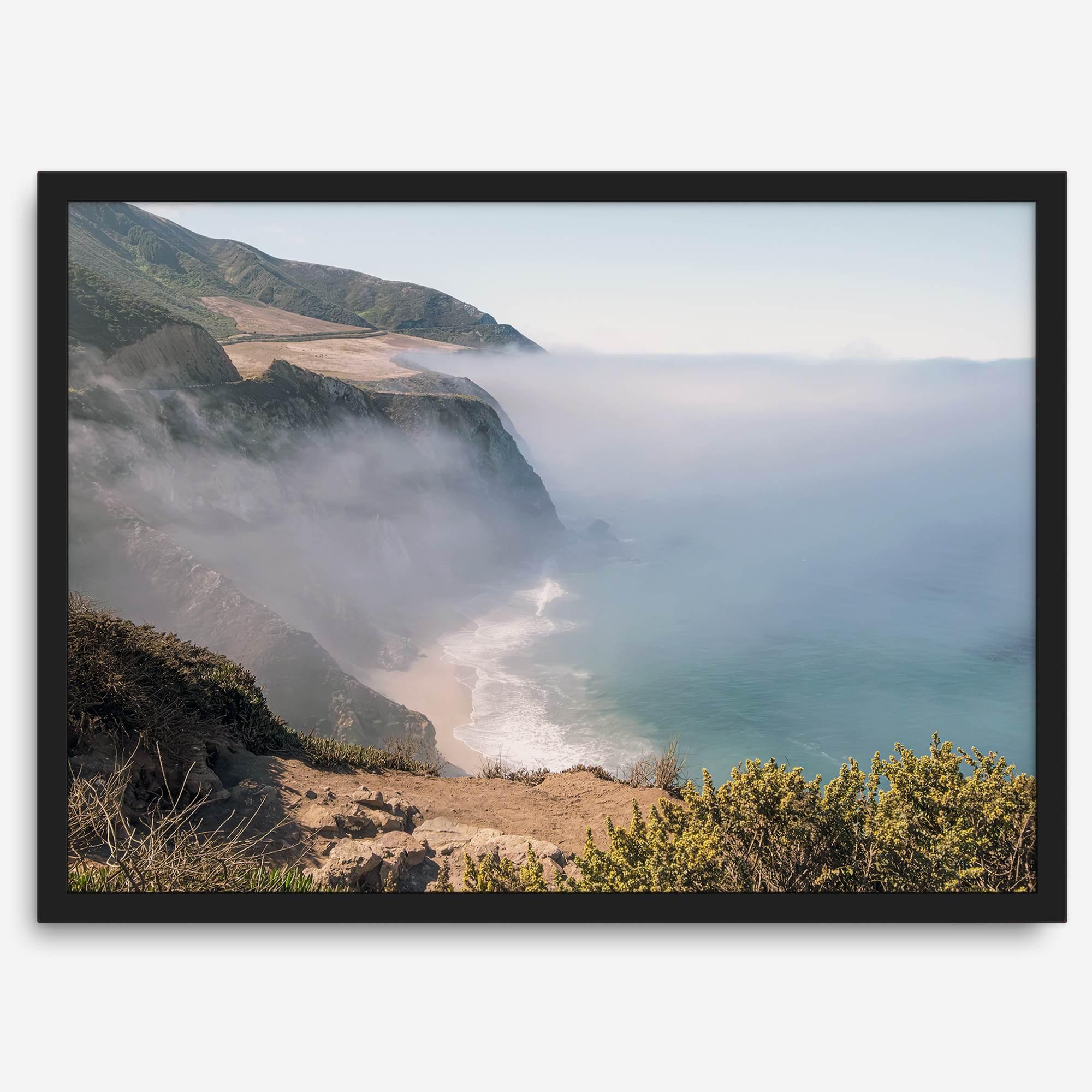 A fine art print of a misty beach in Big Sur, California. Waves crash against the shore as fog drapes over the rugged coastal cliffs, creating a serene, atmospheric scene
