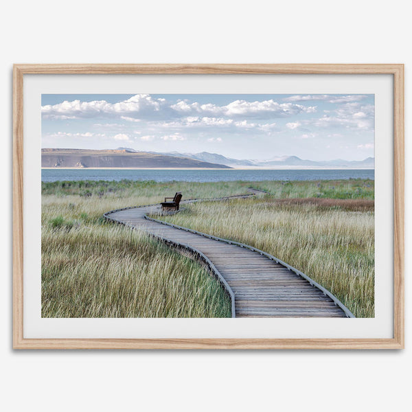 Framed Mono Lake nature photography print featuring a winding boardwalk through tall grasses, leading to a quiet bench beside the lake with mountains in the background.