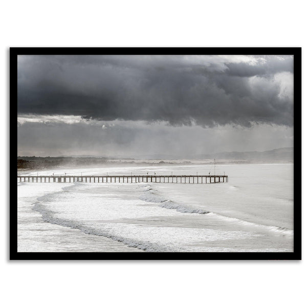 This fine art ocean photography print was taken in Pismo Beach, California, and showcases a distant view of an ocean pier and stormy clouds. Looking long and hard, you can see tens of surfers around the pier.